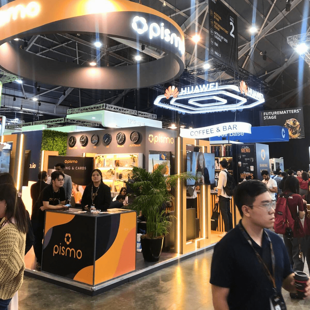 Pismo booth with a coffee and bar section at a fintech event, highlighting their products with clocks displaying global time zones and attendees mingling.